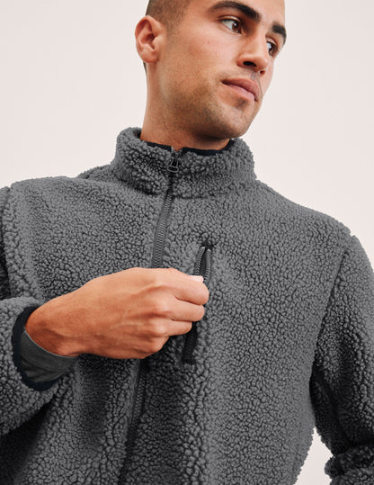 man wearing a gray fleece zip-up jacket against a plain background.