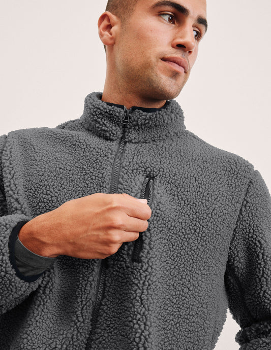man wearing a gray fleece zip-up jacket against a plain background.