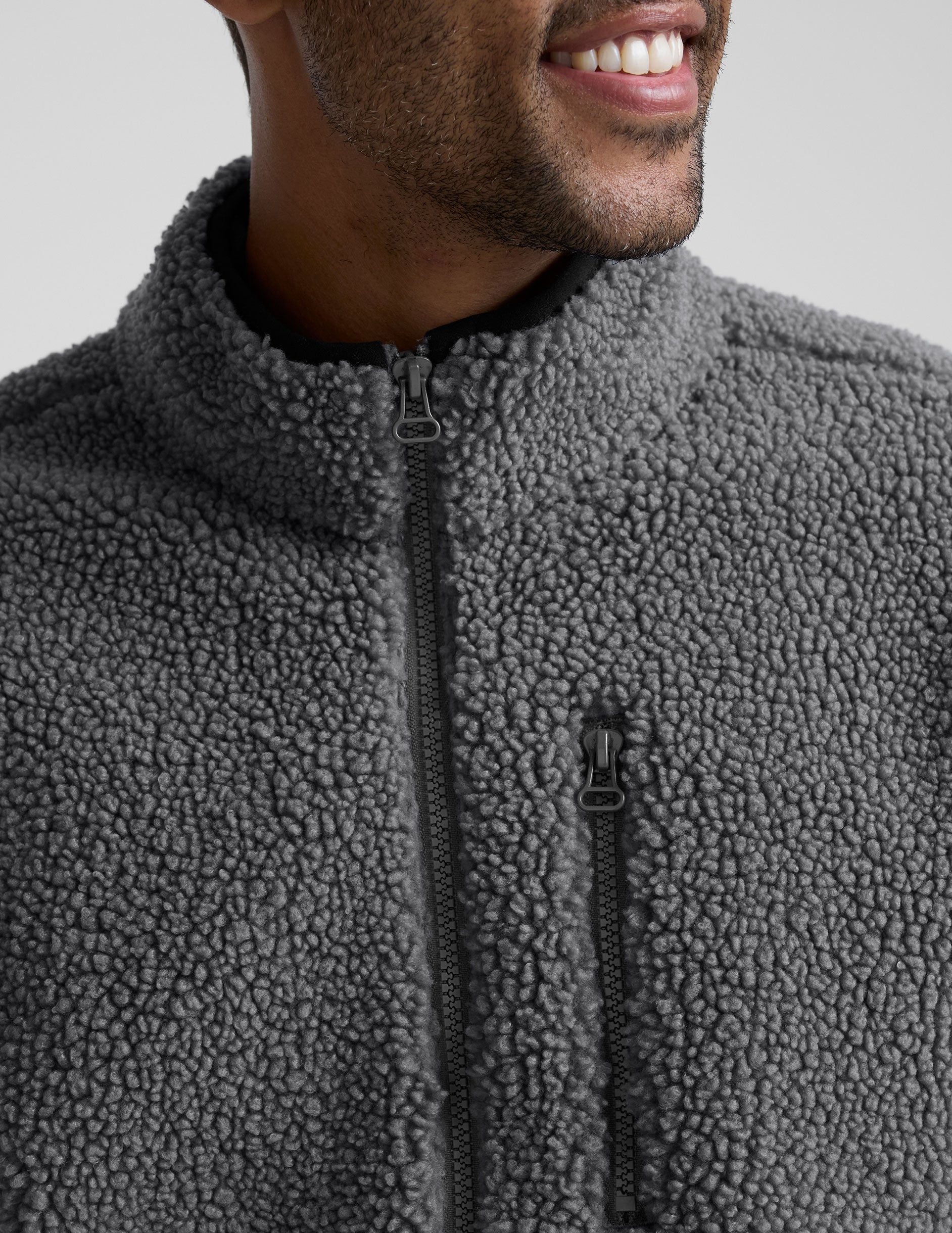 man wearing a gray fleece zip-up jacket against a plain background.
