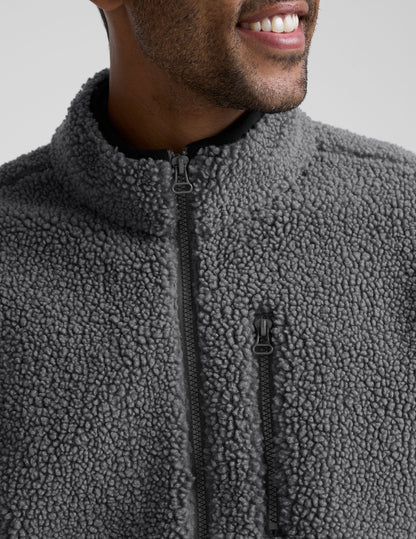 man wearing a gray fleece zip-up jacket against a plain background.