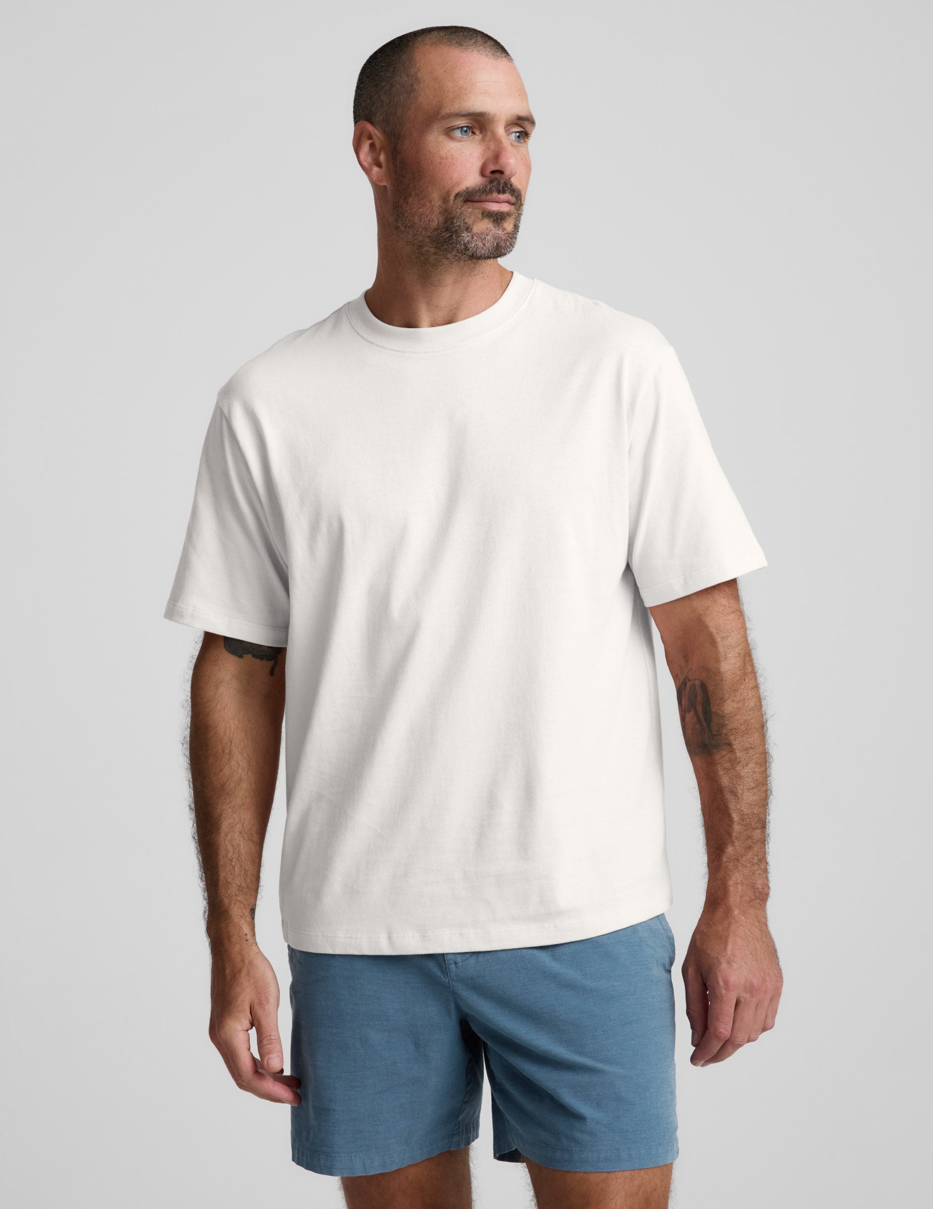 Man wearing a white cotton t-shirt and blue shorts on a light gray background.