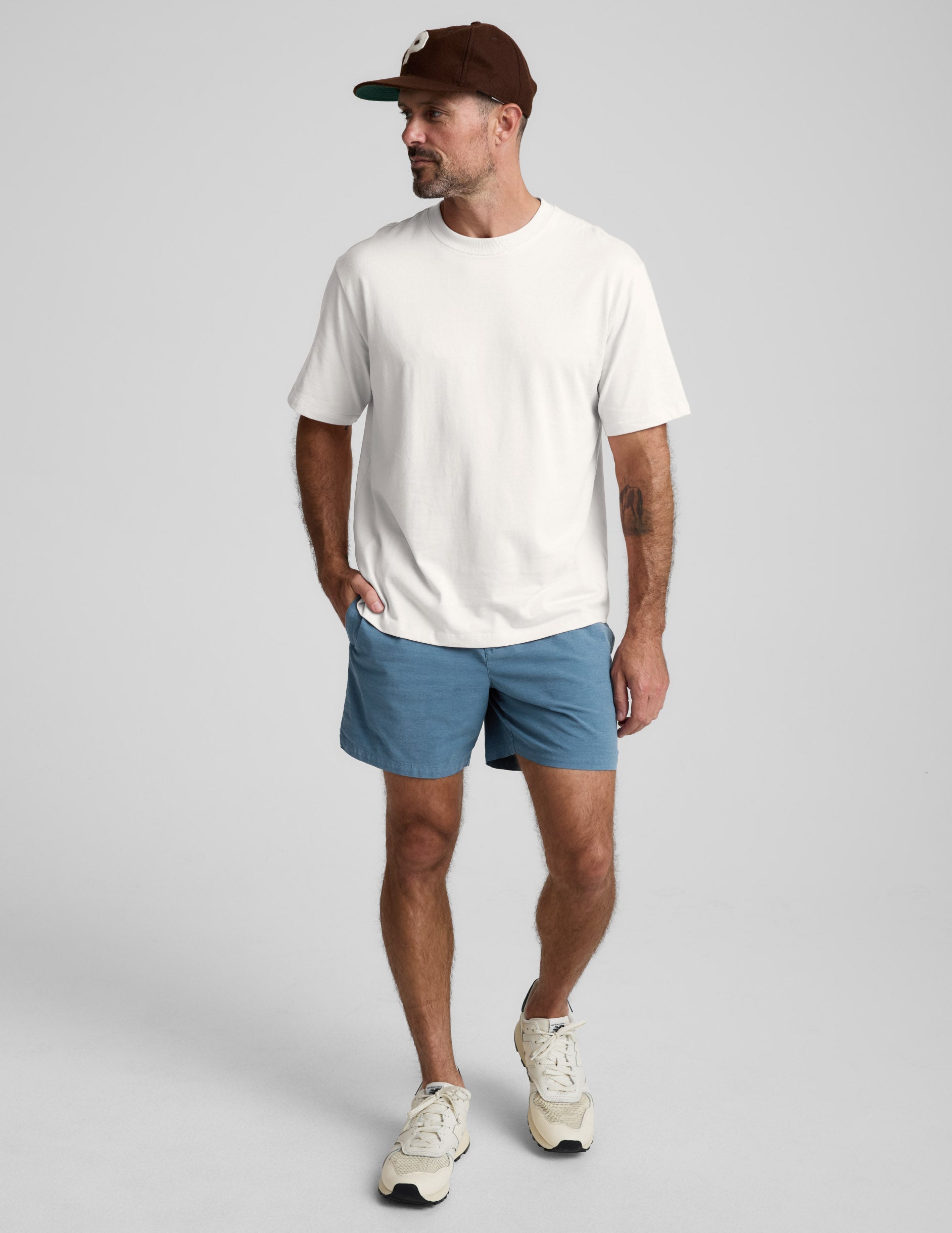 Man wearing a white cotton t-shirt and blue shorts on a light gray background.
