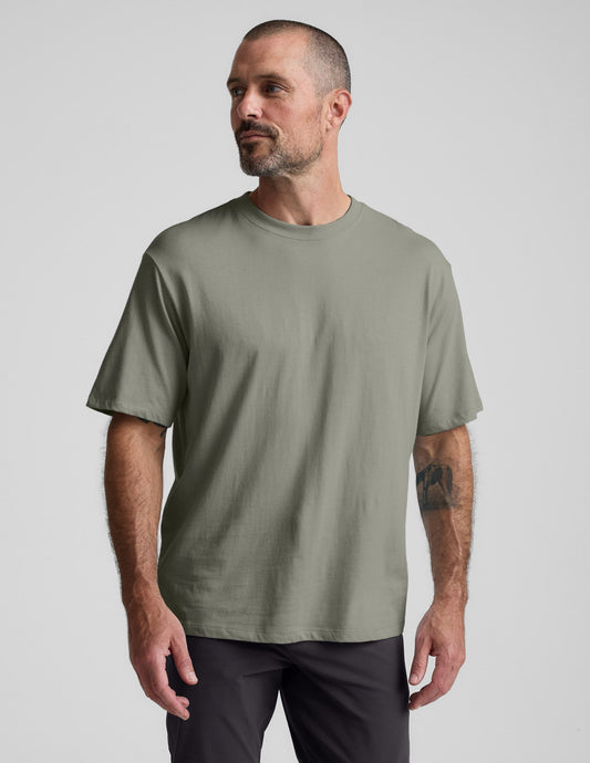 Man wearing a green cotton t-shirt and black pants against a plain background.