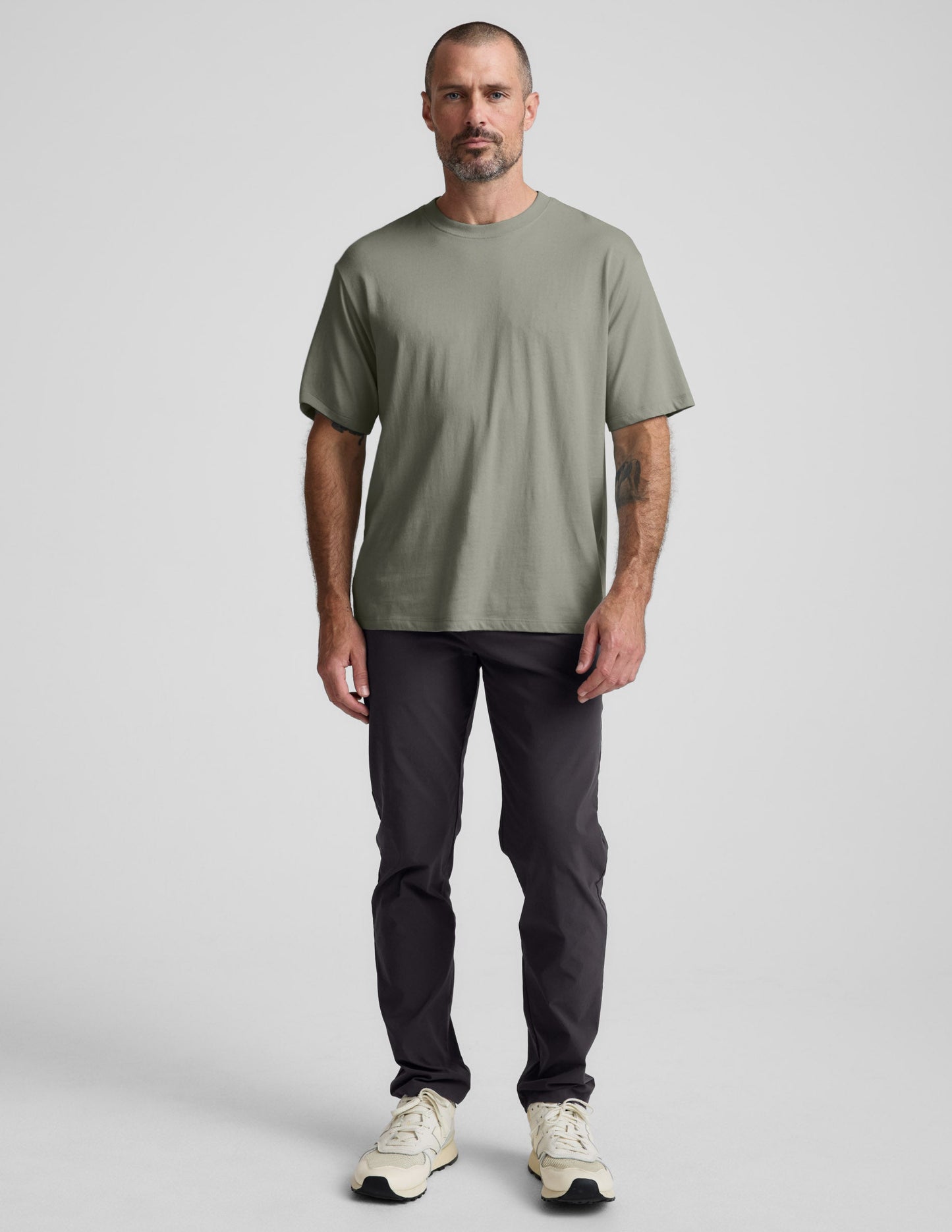 Man wearing a green cotton t-shirt and black pants against a plain background.