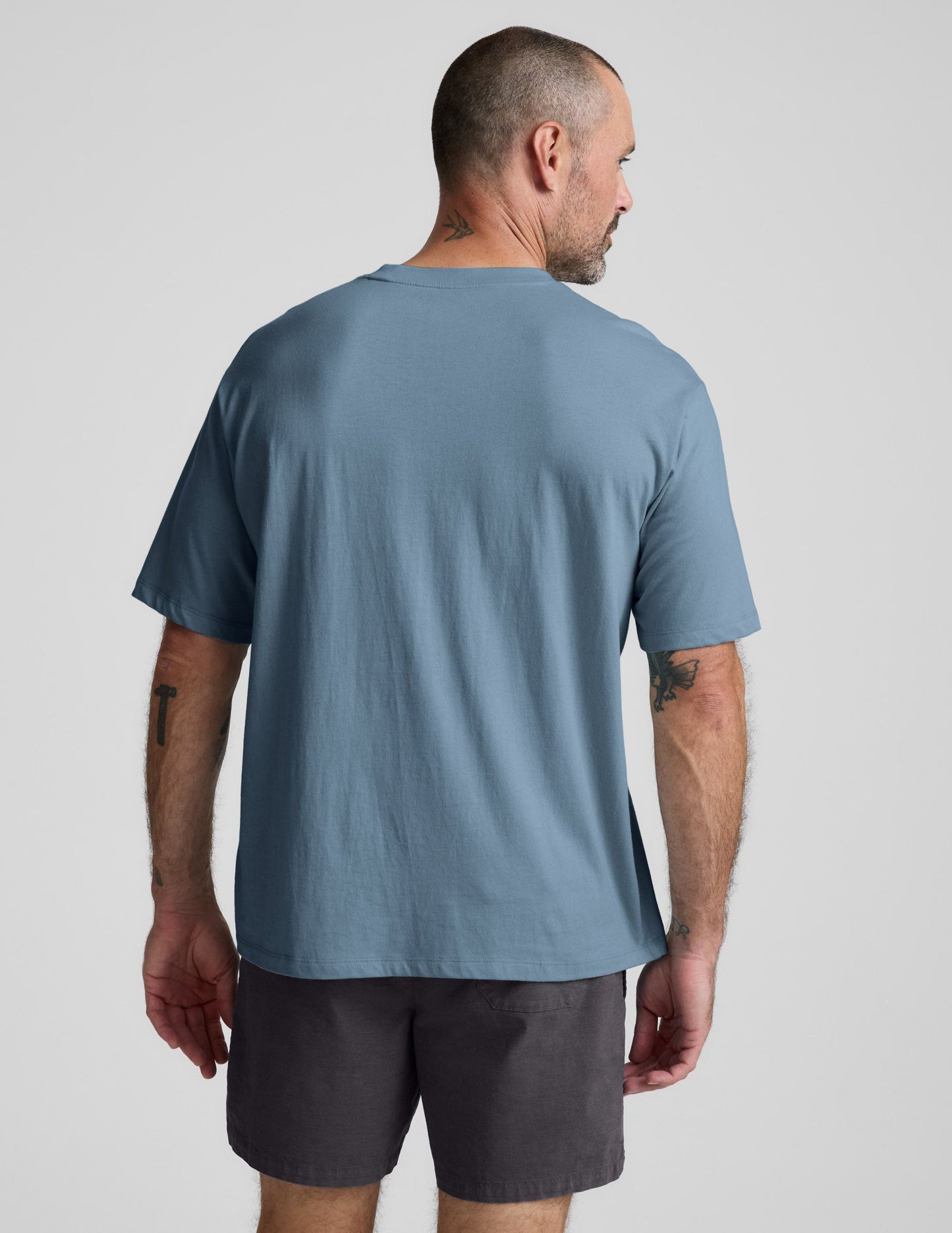 Man wearing a blue cotton t-shirt and gray shorts against a plain background.