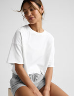 Woman wearing a white cropped t-shirt and gray fleece shorts against a plain background.