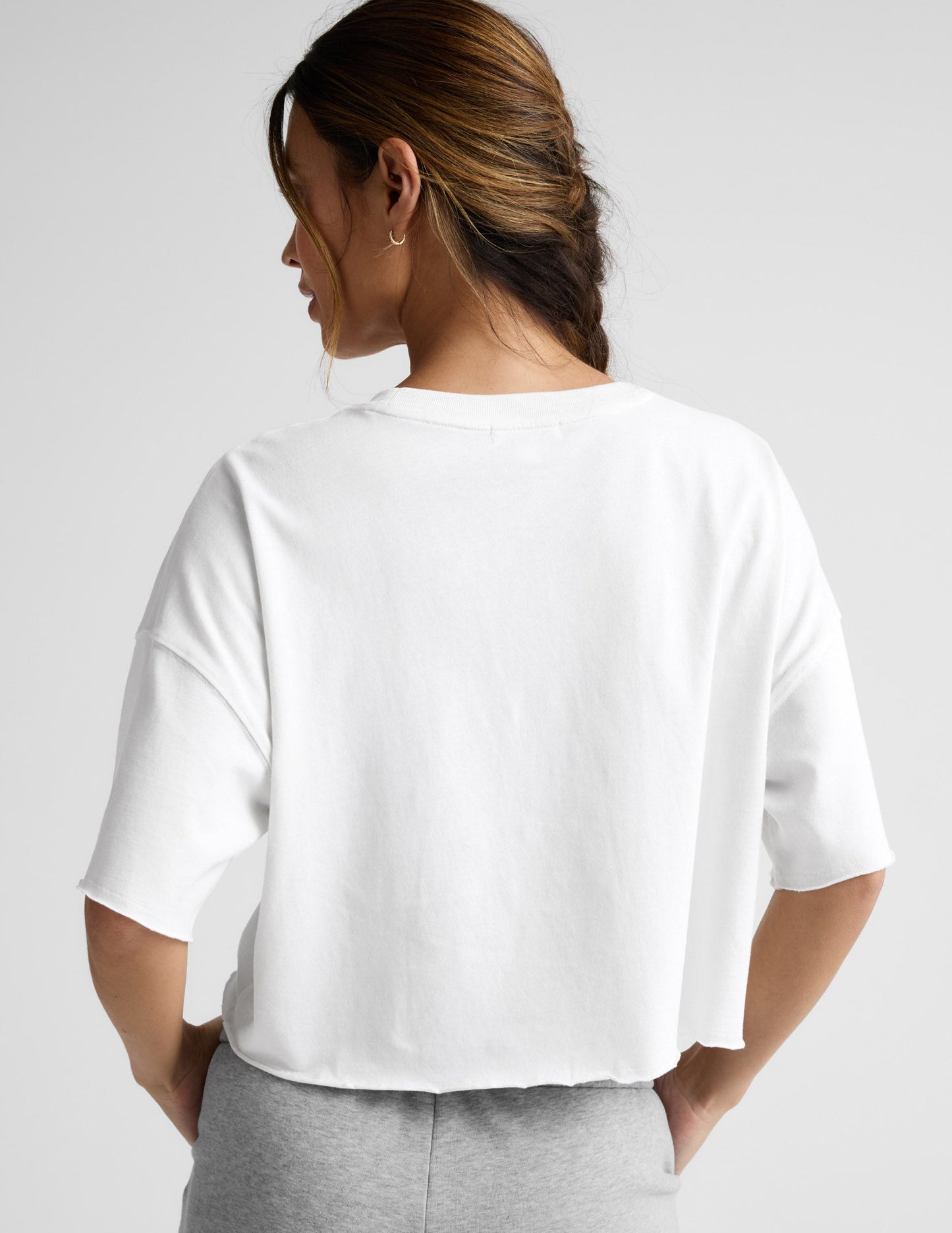Woman wearing a white cropped t-shirt and gray fleece shorts against a plain background.
