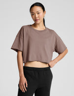 Woman wearing a brown cropped top and black pants on a light gray background.