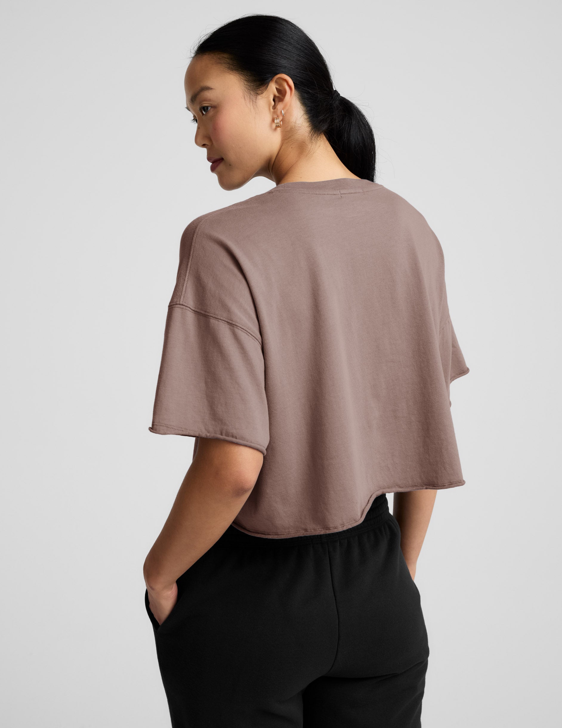 Woman wearing a brown cropped top and black pants on a light gray background.