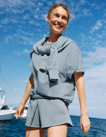 Woman wearing a blue t-shirt and shorts in front of the ocean.