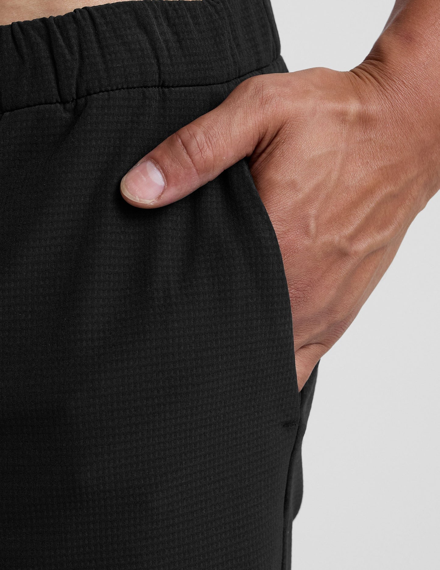 Close-up of black Dynamic Men's Straight Leg Pant featuring textured fabric, elastic waistband, and a hand in the pocket.