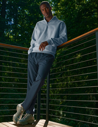 Man in a forest leans on a balcony wearing navy Dynamic Men's Straight Leg Pant and a light blue sweatshirt.