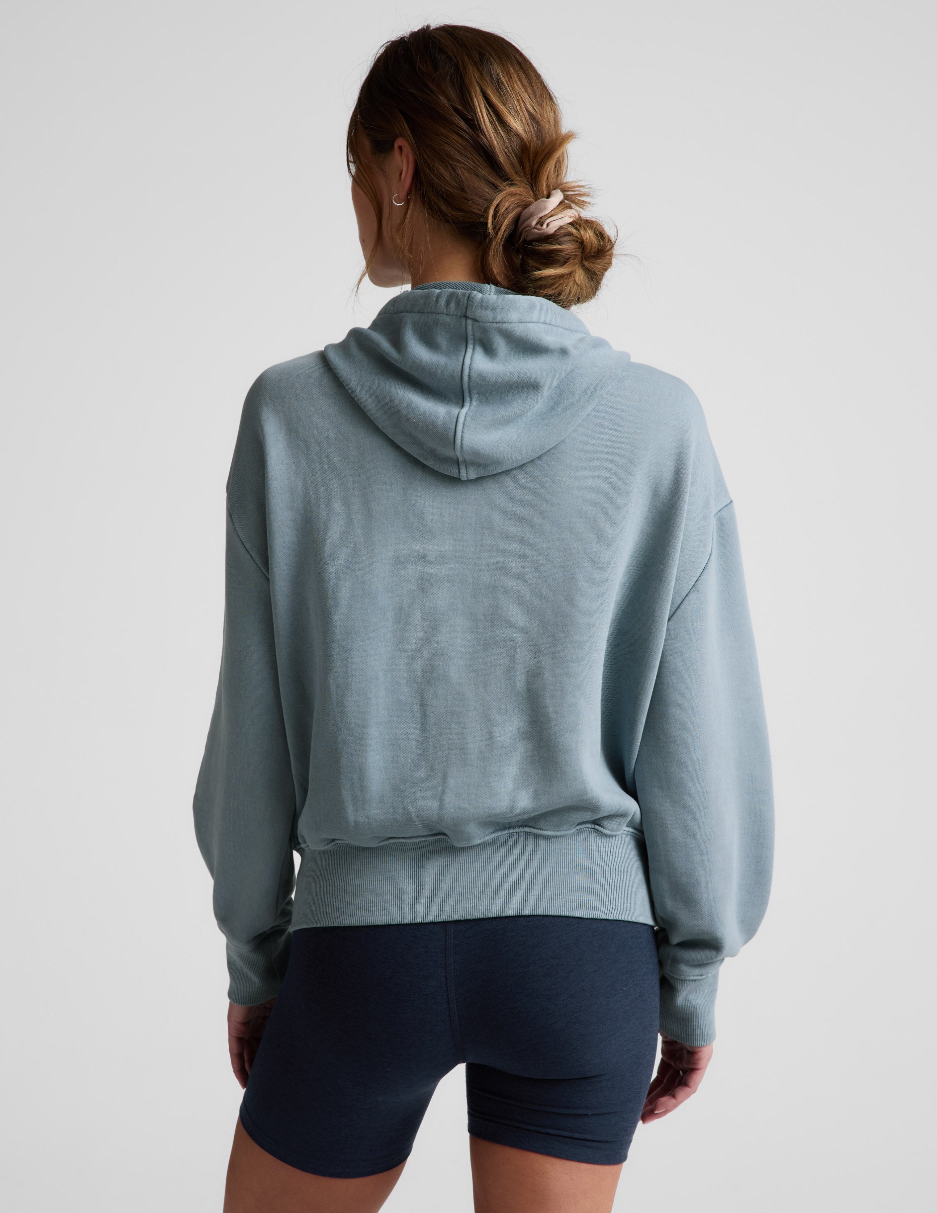 Woman wearing a blue zip-up jacket and blue biker shorts against a plain background.