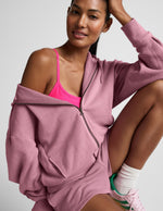 Woman wearing a pink hoodie and sports bra with a neutral background.