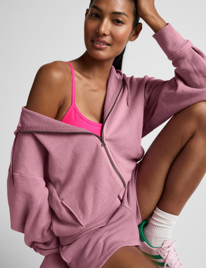Woman wearing a pink hoodie and sports bra with a neutral background.