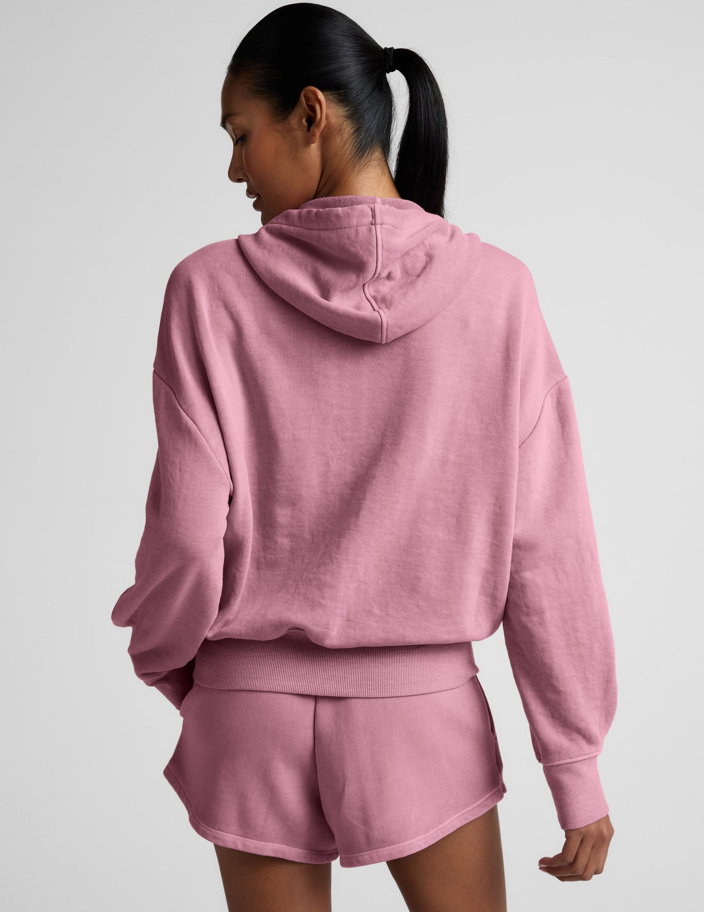 Woman wearing a pink zip-up hoodie and shorts set on a neutral background.