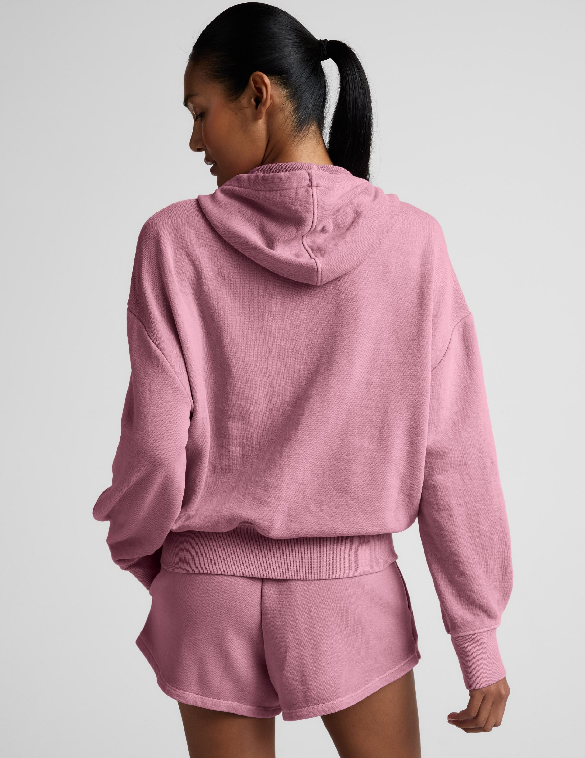 Woman wearing a pink zip-up hoodie and shorts set on a neutral background.