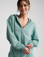 Woman wearing a green zip-up sweatshirt and green shorts against a plain background.