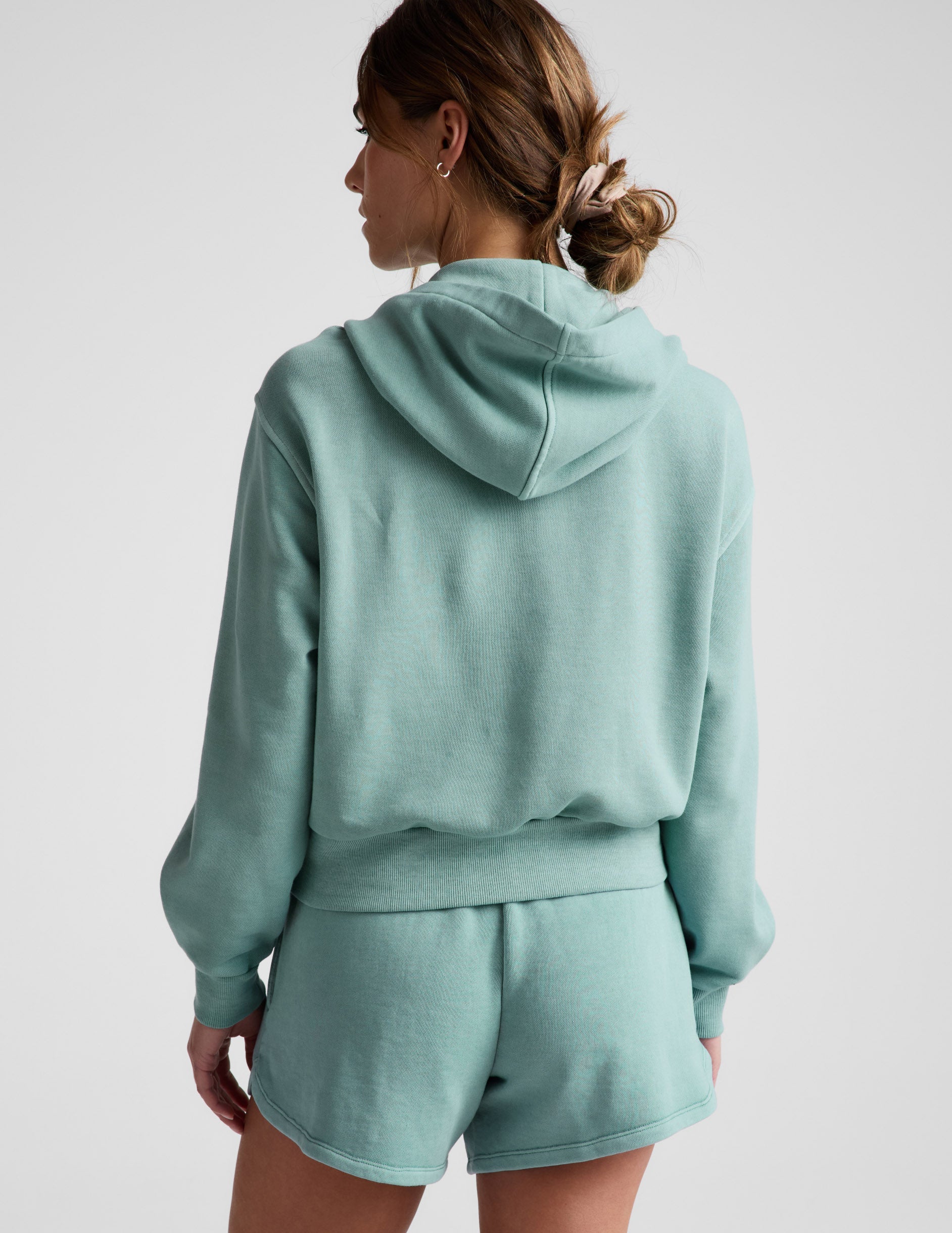 Woman wearing a green zip-up sweatshirt and green shorts against a plain background.