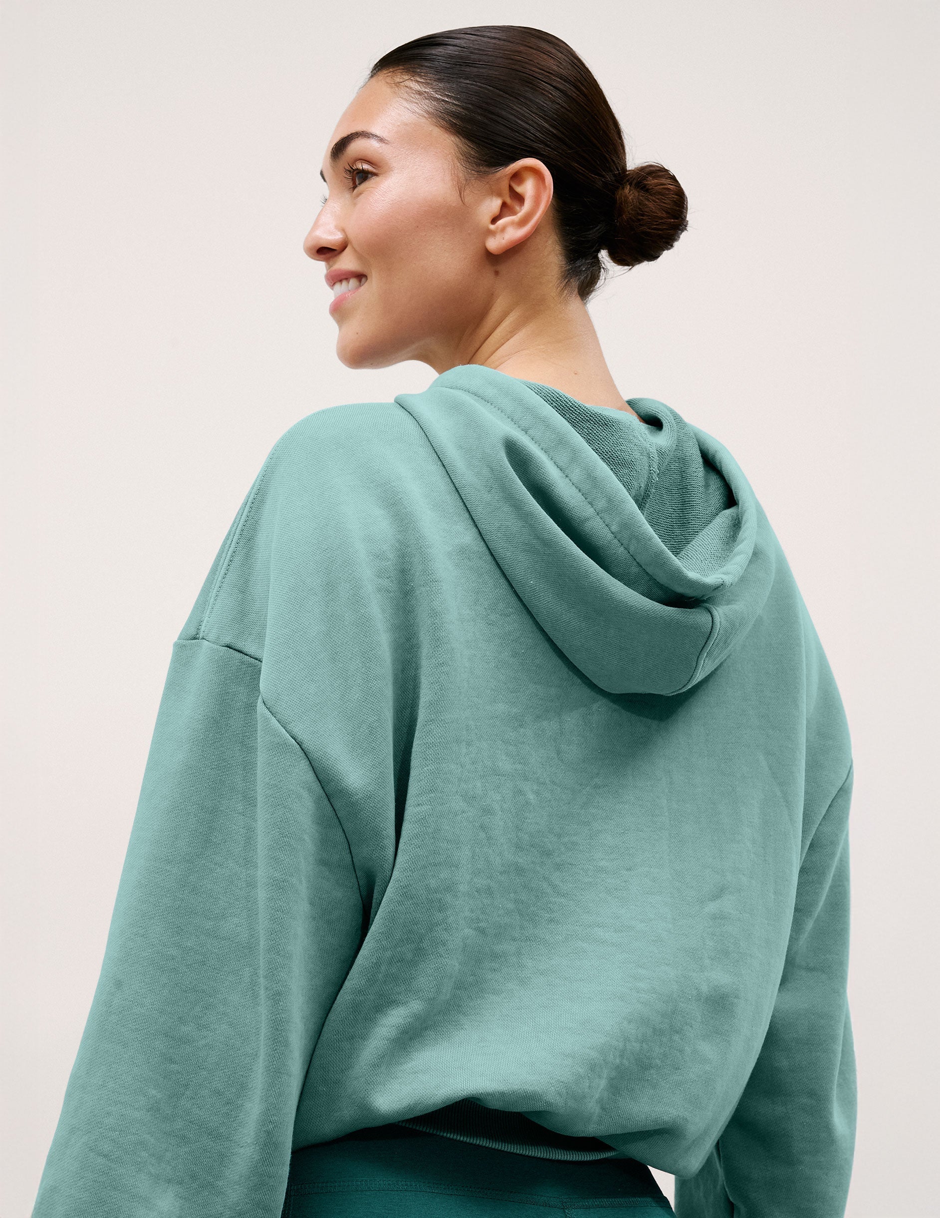 Woman wearing a teal hoodie against a plain background.