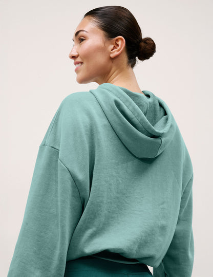 Woman wearing a teal hoodie against a plain background.