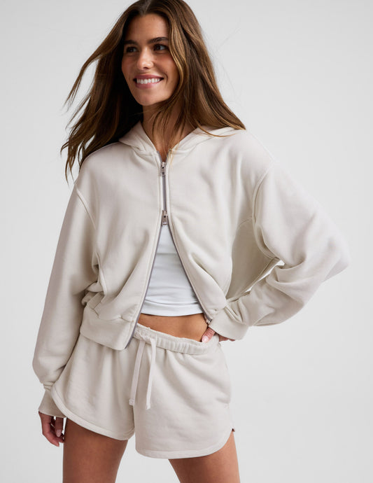 Woman wearing a white sweatshirt and shorts on a plain background.
