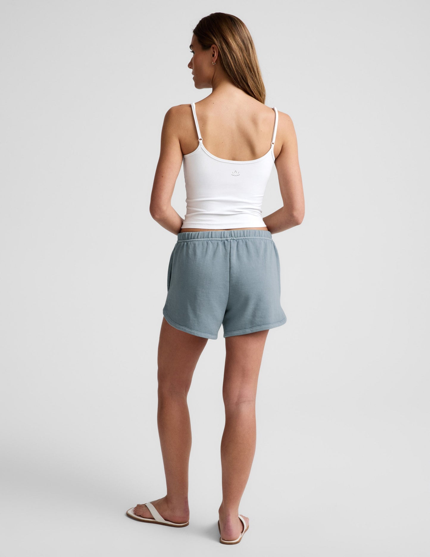 Back view of a woman wearing the blue Fade Out Mid-Rise Short with curved hems and a white camisole.