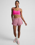 Smiling model wearing pink Fade Out Mid-Rise Short with curved hems and side pockets against a neutral studio background.