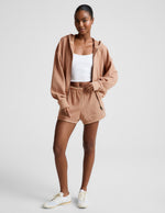 Woman wearing Tan Fade Out Mid-Rise Short™ with a white tank top and matching hoodie featuring a curved hem.