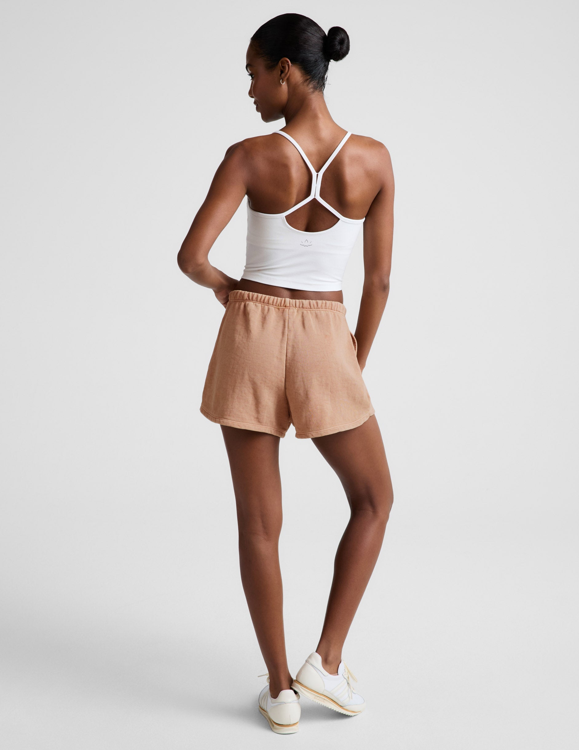 Woman wearing Cream Fade Out Mid-Rise Short™ paired with a white racerback tank top and white sneakers. Rear view.