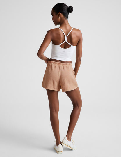 Woman wearing Cream Fade Out Mid-Rise Short™ paired with a white racerback tank top and white sneakers. Rear view.