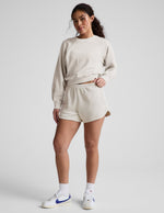 Cream Fade Out Mid-Rise Short featuring a gathered elastic waistband and curved dolphin hem, worn with matching sweatshirt.