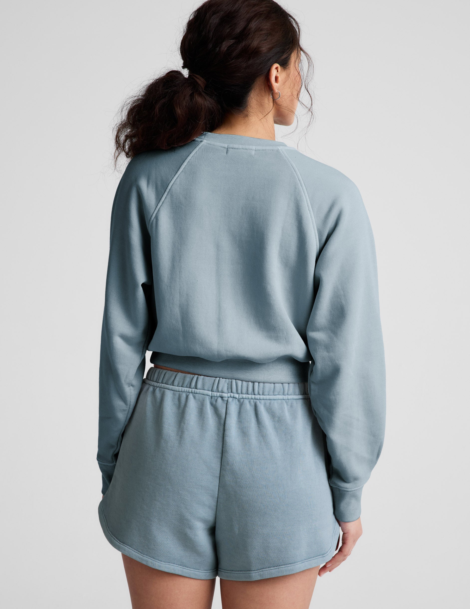 Woman wearing a blue crew-neck sweatshirt and shorts against a plain background.