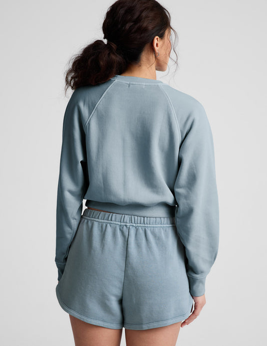 Woman wearing a blue crew-neck sweatshirt and shorts against a plain background.