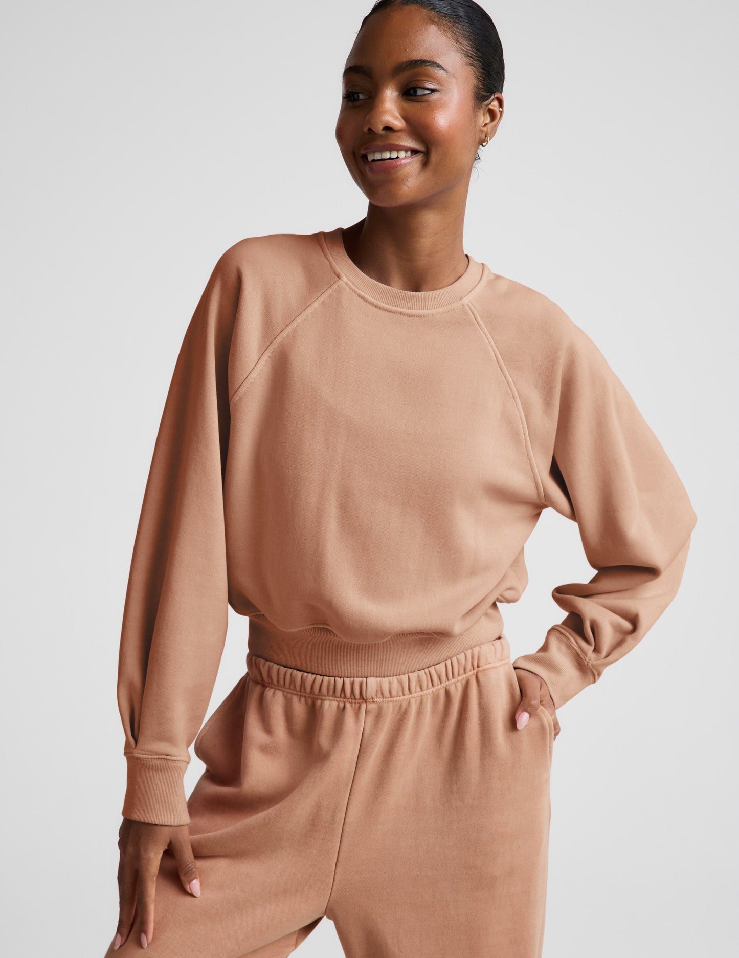 Woman wearing a beige sweatshirt and pants set on a plain background.