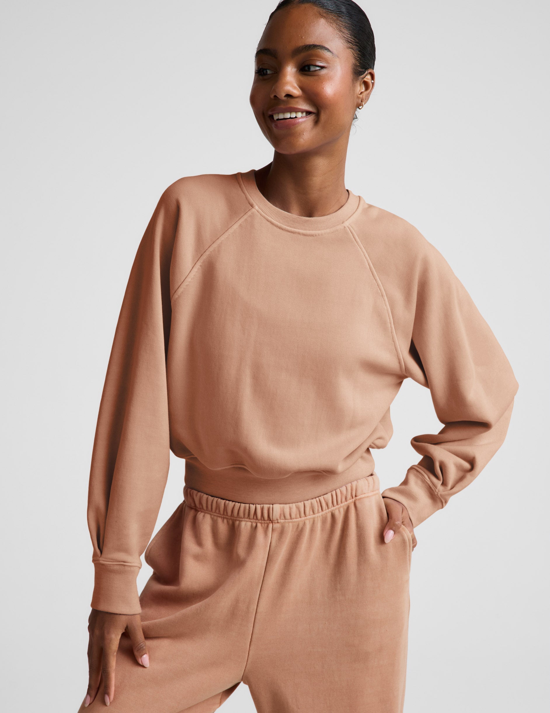 Woman wearing a beige sweatshirt and pants set on a plain background.