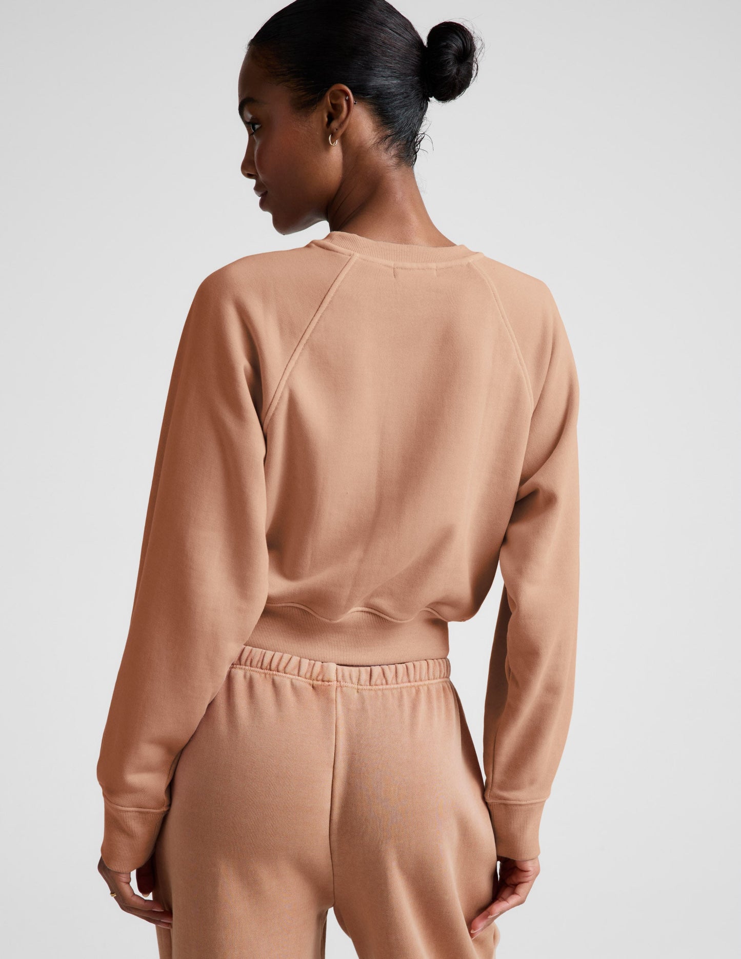Woman wearing a beige sweatshirt and pants set on a plain background.