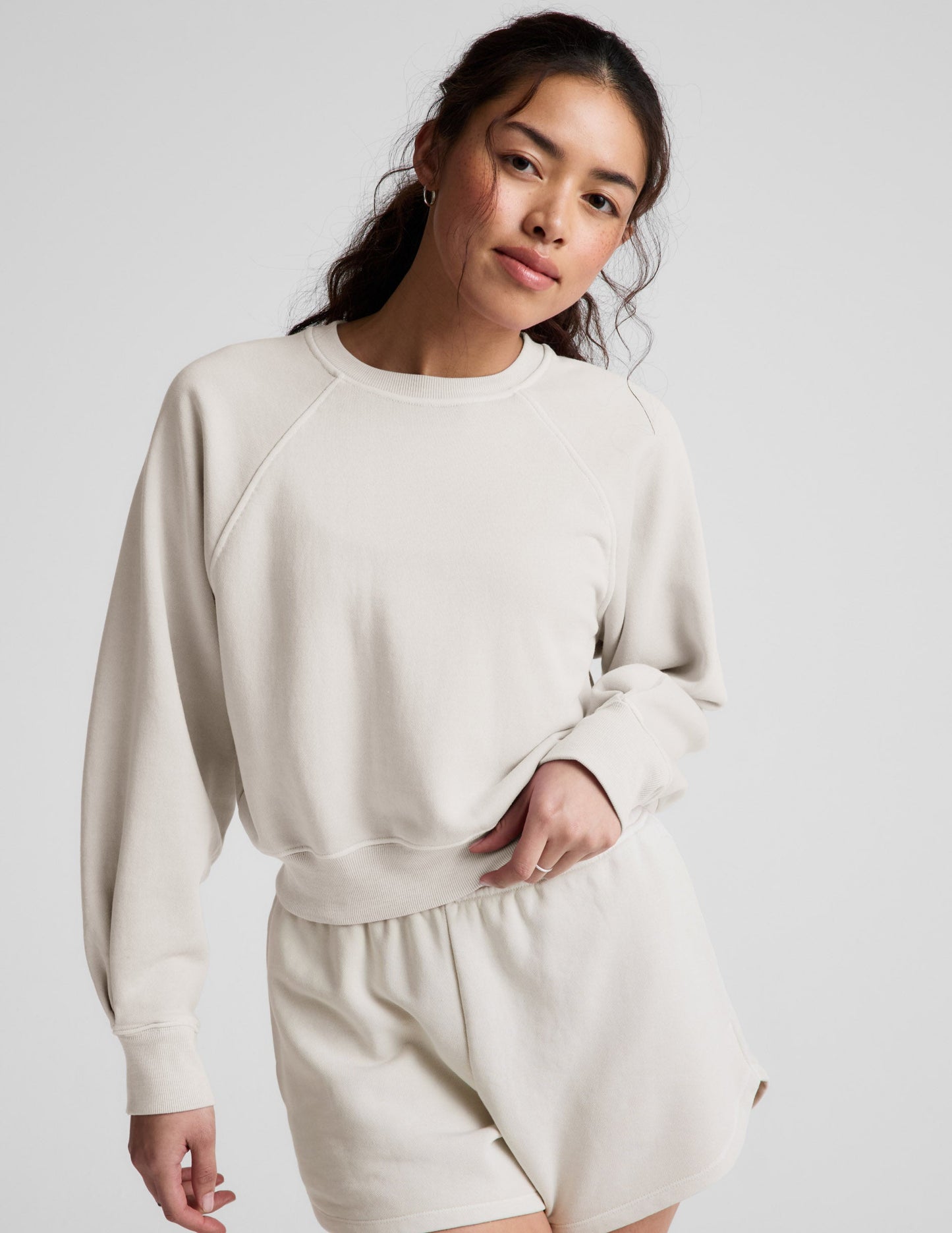 Woman wearing a white crew-neck and shorts against a plain background.