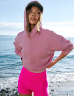 Woman wearing a pink hoodie and shorts standing on the beach.
