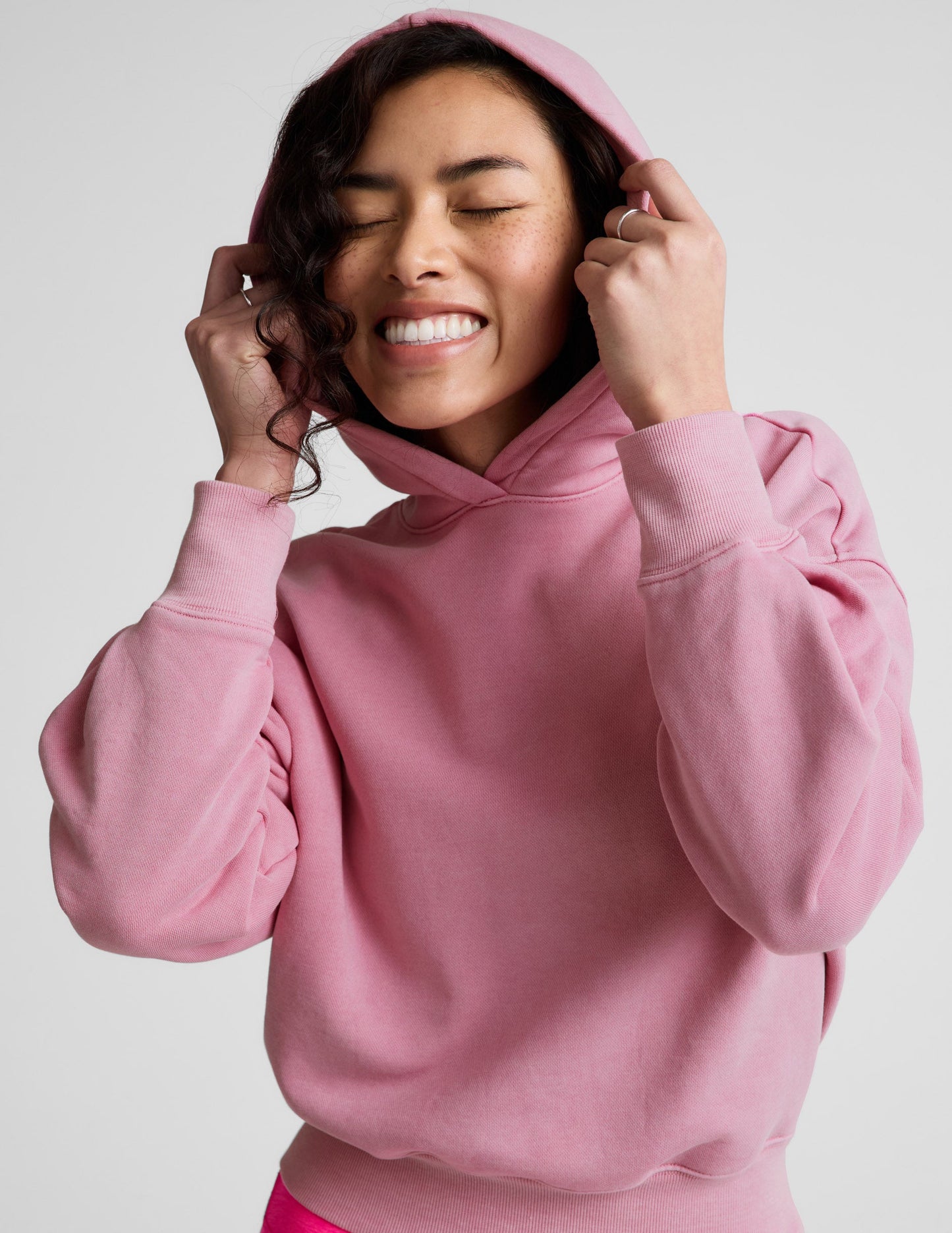 Woman wearing a pink sweatshirt and bright pink shorts on a plain background.