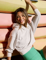 Woman wearing a white hoodie and green shorts sitting in front of kayaks.