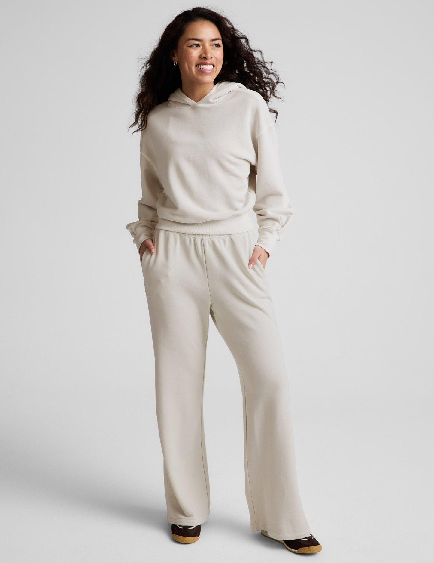 Woman wearing a white hoodie and pants against a plain background.