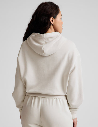 Woman wearing a white hoodie and pants against a plain background.