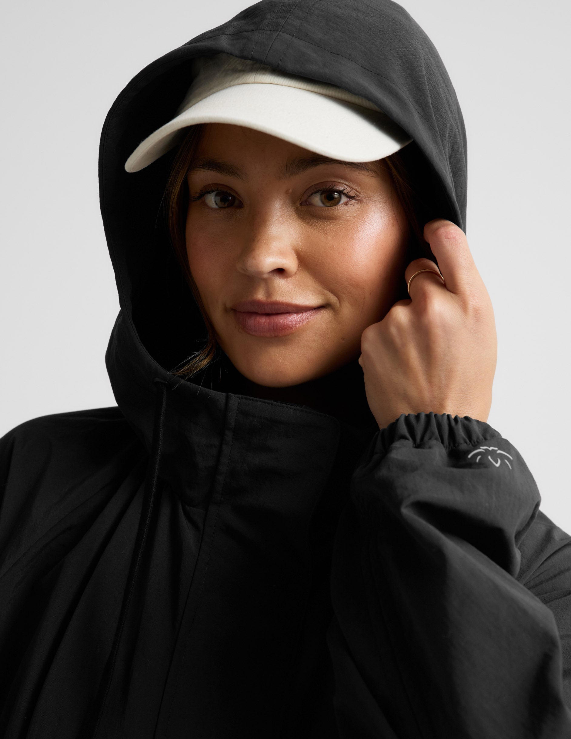 Woman wearing a black trench coat over a gray sports bra and leggings on a plain background.