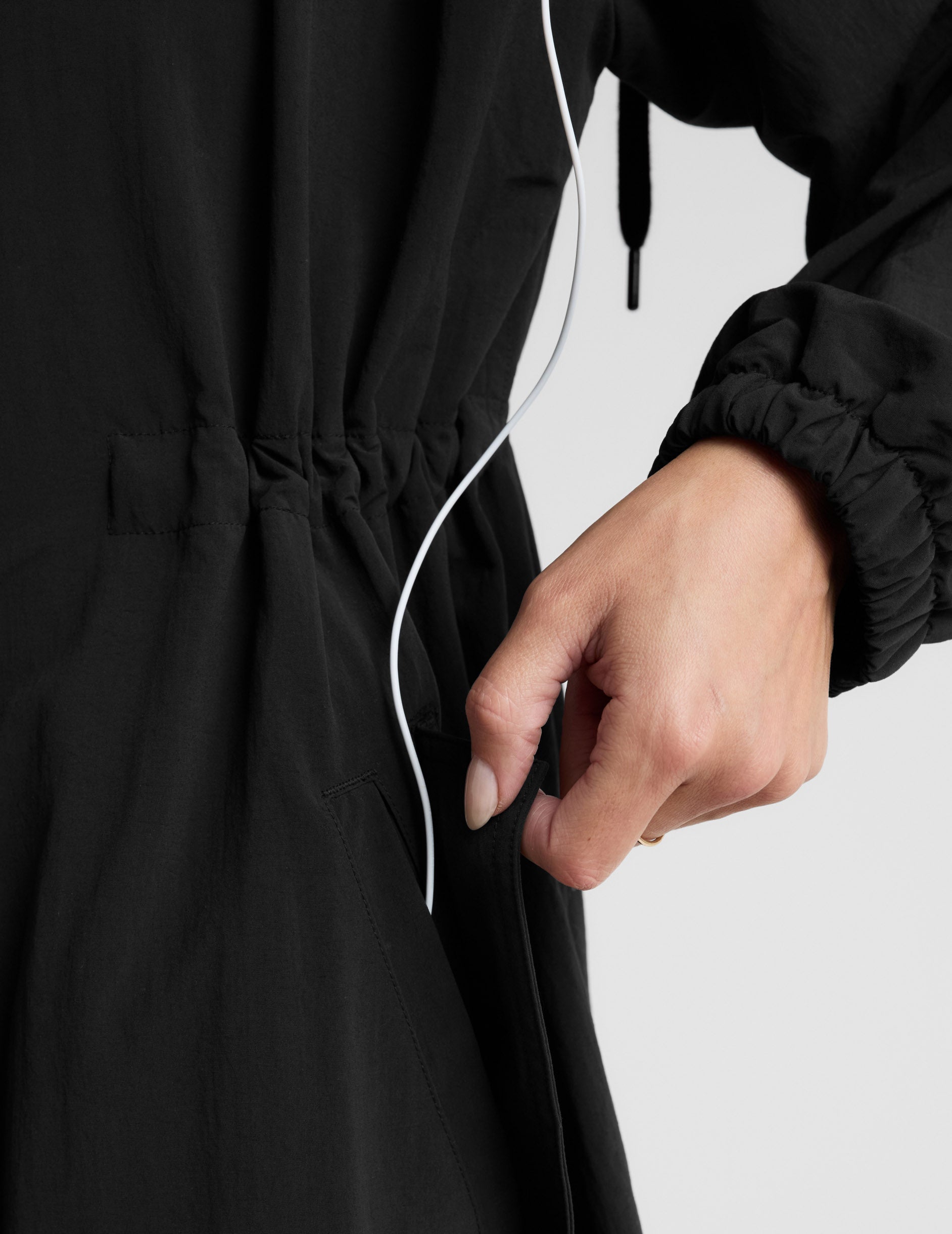 Woman wearing a black trench coat over a gray sports bra and leggings on a plain background.