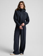 Woman wearing a blue hooded jain jacket and pants against a plain background.