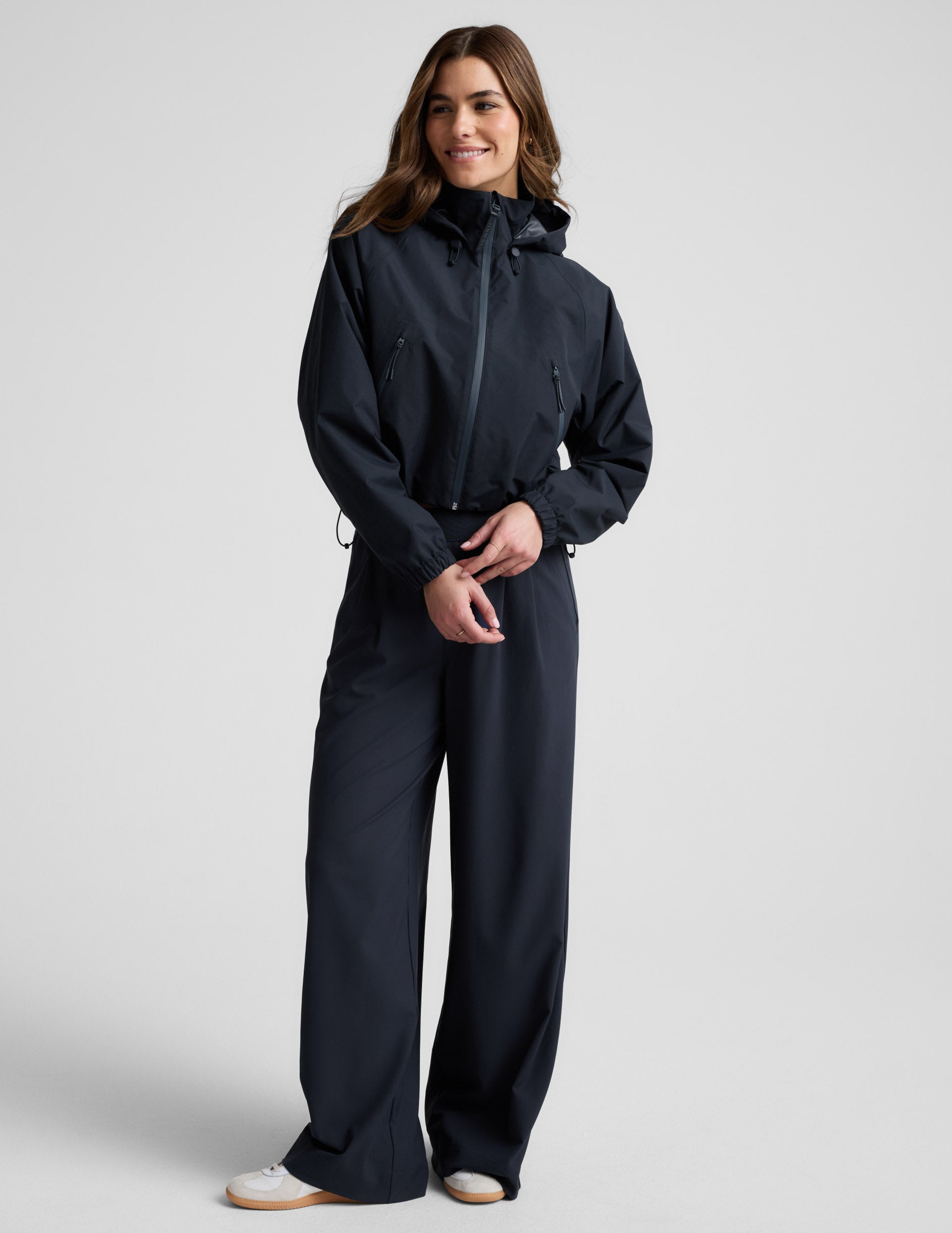 Woman wearing a blue hooded jain jacket and pants against a plain background.