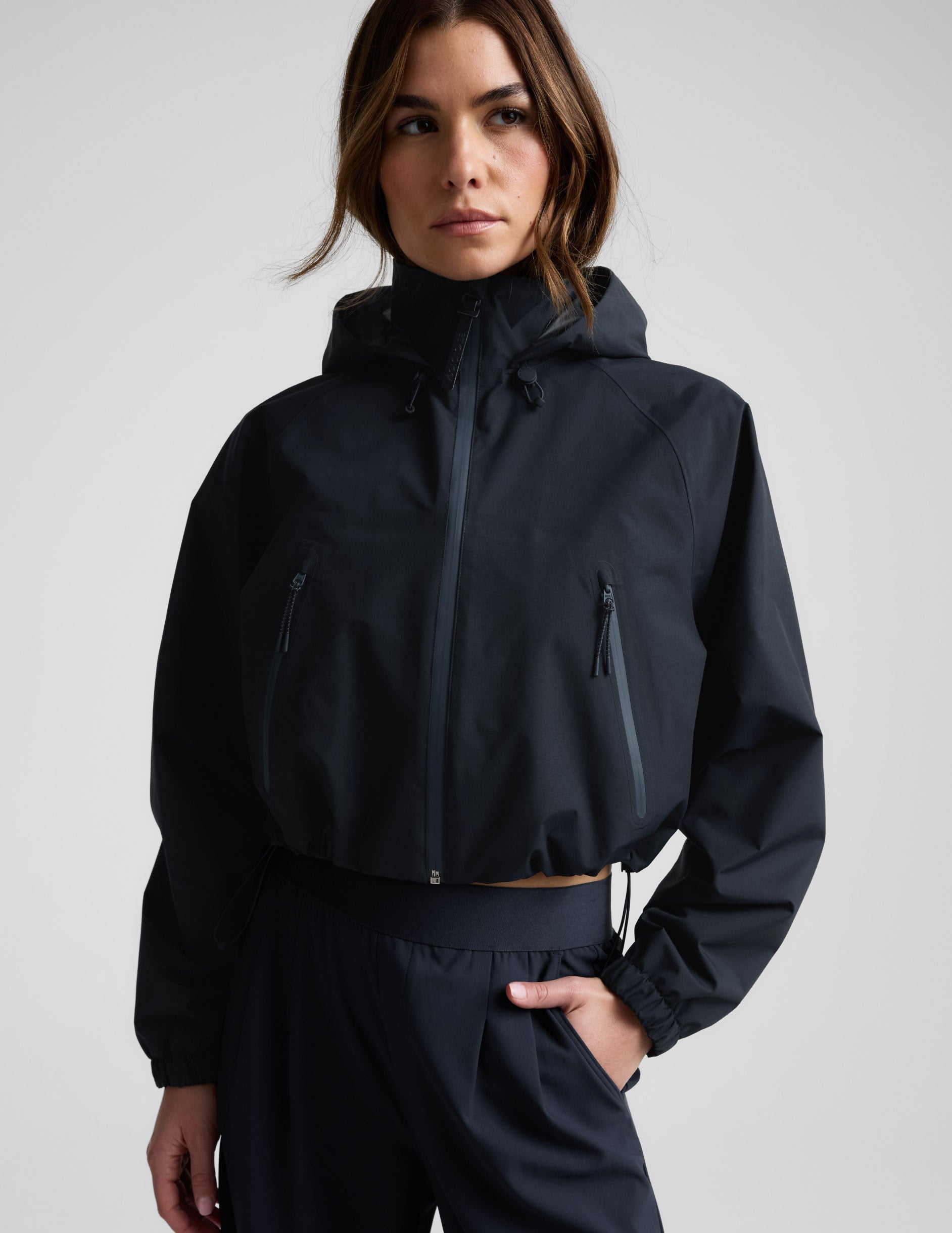 Woman wearing a blue hooded jain jacket and pants against a plain background.
