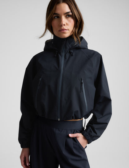 Woman wearing a blue hooded jain jacket and pants against a plain background.
