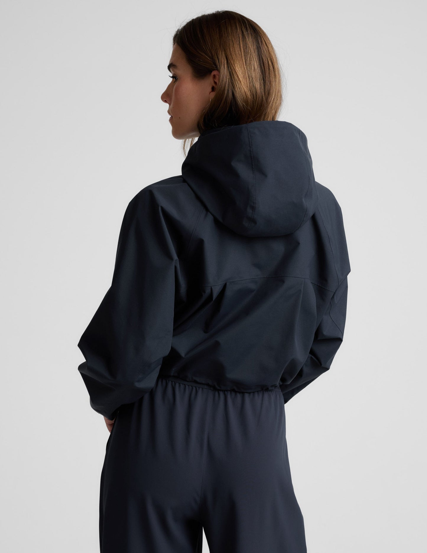 Woman wearing a blue hooded jain jacket and pants against a plain background.